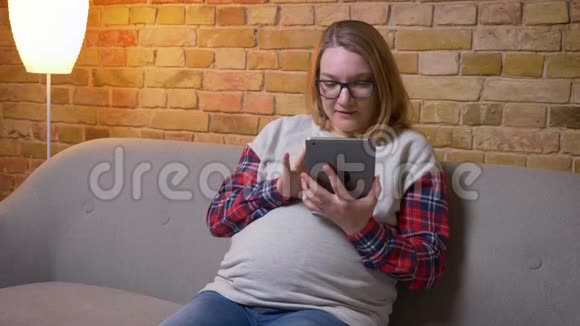 年轻怀孕女性使用平板电脑的特写镜头并在坐在沙发上拍摄绿色屏幕视频的预览图