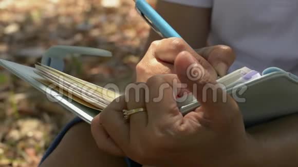 夏天在公共公园的树荫下紧紧地抓住坐着写日记的女人的手视频的预览图