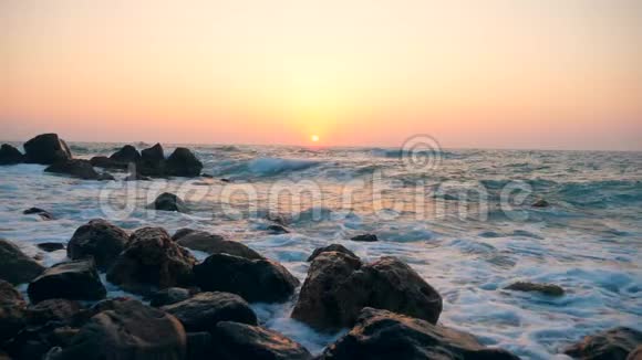 海浪在日落背景下撞击海滩上的石头动作缓慢视频的预览图