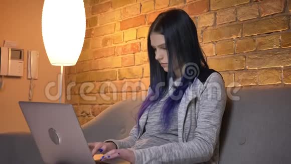 年轻漂亮的白种人女性在坐在沙发上用笔记本电脑打字的特写镜头视频的预览图