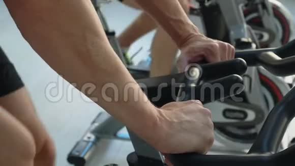 在健身室里男性手拿室内自行车人在健身房的自行车课上旋转自行车健身男子训练视频的预览图