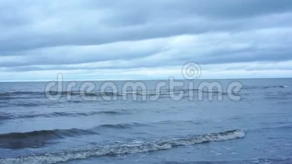 平静的蓝色海浪和白色泡沫翻滚在沙滩上视频的预览图