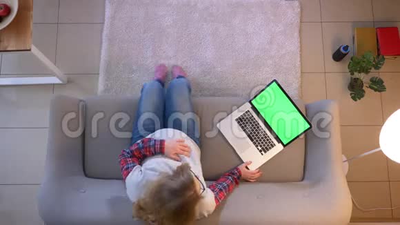 年轻孕妇坐在沙发上用绿色屏幕浏览笔记本电脑的特写镜头视频的预览图