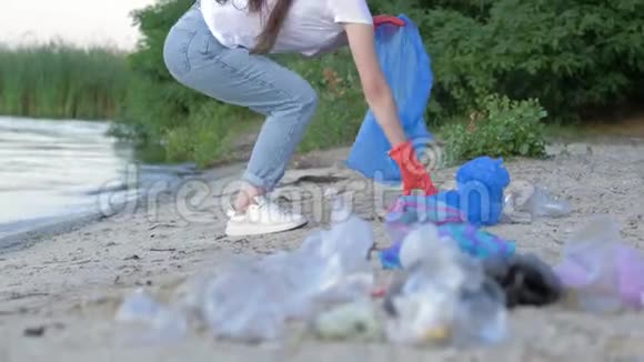 海滩清洁活动积极分子女性戴着橡胶手套在清理河堤时在垃圾袋中收集塑料垃圾视频的预览图