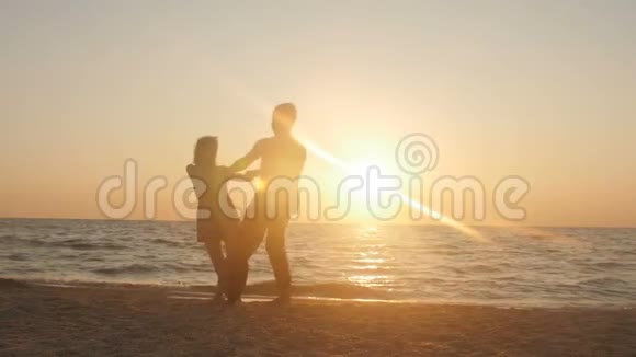 浪漫的年轻夫妇在海滩上男人在日落时搂着他的女朋友在美丽的海边玩得开心视频的预览图