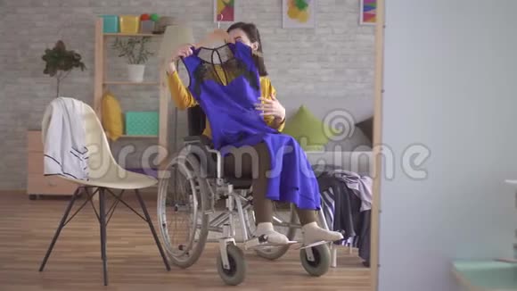 坐轮椅的年轻残疾女孩在现代公寓里为约会挑选衣服视频的预览图