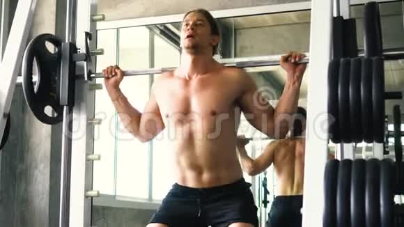 肌肉男在健身房的机器上做杠铃蹲运动视频的预览图
