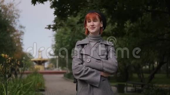 秋天的一天一个年轻迷人的红头发短发女孩穿着黑色贝雷帽和灰色外套在一个自然公园里视频的预览图