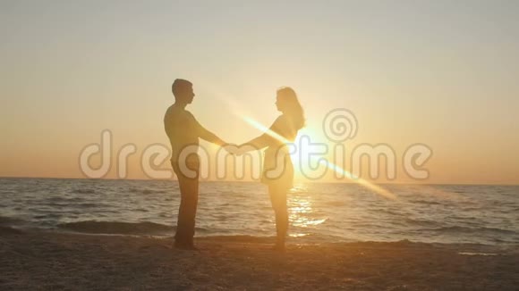 浪漫的年轻夫妇在海滩上男人在日落时搂着他的女朋友在美丽的海边玩得开心视频的预览图