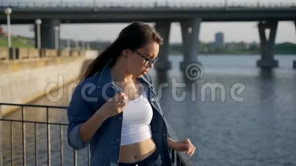 一个戴眼镜的年轻女孩站在城市海湾的栏杆附近视频的预览图