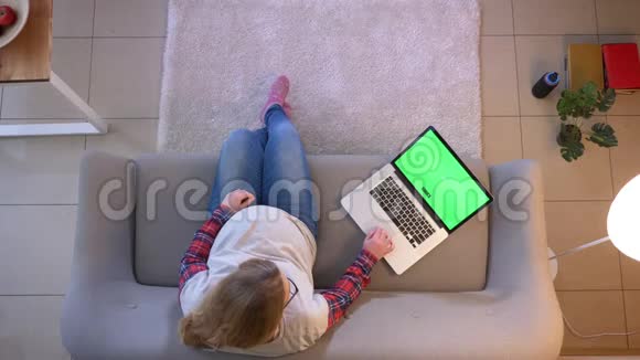年轻孕妇坐在室内沙发上用绿色屏幕浏览笔记本电脑的特写镜头视频的预览图
