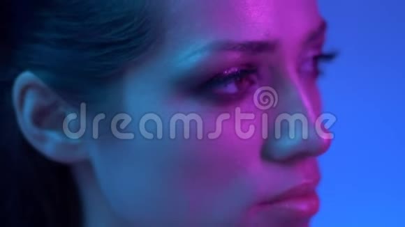 明亮的时尚模特在彩色紫色和蓝色霓虹灯的轮廓在工作室向右观看视频的预览图