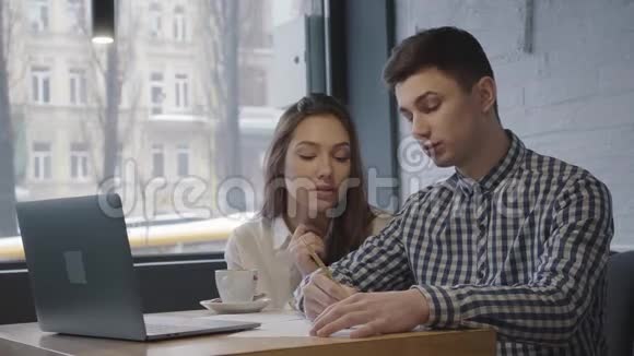 年轻夫妇一起在现代咖啡馆工作自信的男人向女孩解释并写在上面视频的预览图