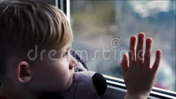 一个漂亮的金发小男孩望着阳光明媚的窗外等着爸爸下班回家视频的预览图