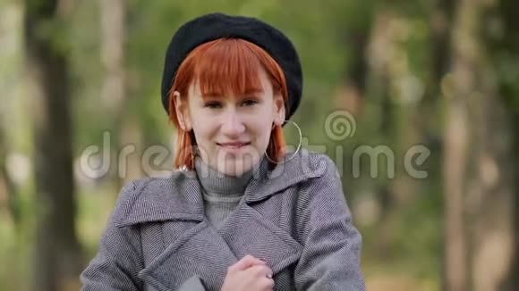 秋天的一天一个年轻迷人的红头发短发女孩穿着黑色贝雷帽和灰色外套在一个自然公园里视频的预览图