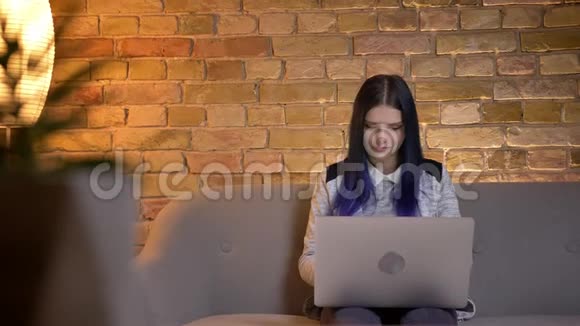 年轻迷人的白种人潮女的特写镜头她染着头发在笔记本电脑上打字坐在沙发上视频的预览图