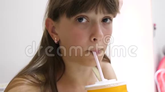 女孩喝美味的水果鸡尾酒从吸管坐在咖啡馆特写视频的预览图