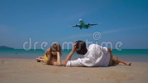 一位快乐的男女游客躺在美丽的海滩上观看着一架降落的飞机视频的预览图