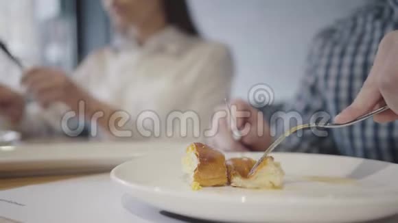无法辨认的夫妇在现代咖啡馆里吃东西前景中的人用叉子和刀吃馅饼模糊不清视频的预览图