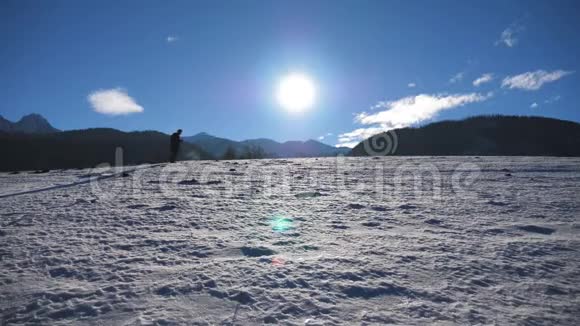 在阳光明媚的日子里一个面目全非的家伙在雪地草地上用棍子走路年轻的徒步旅行者在雪地上跋涉视频的预览图