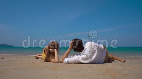 一位快乐的男女游客躺在美丽的海滩上观看着一架降落的飞机视频的预览图