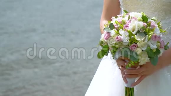 新娘在流动的水背景上捧着一束白色和粉红色的玫瑰手和花束的特写移动框架视频的预览图