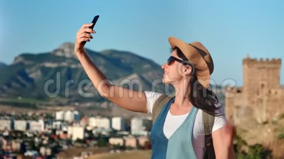 快乐女旅行者在山景上摆姿势用智能手机自拍视频的预览图
