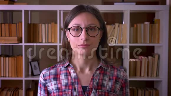 一位戴眼镜的年轻有魅力女学生的特写镜头她竖起大拇指看着图书馆里微笑的镜头视频的预览图