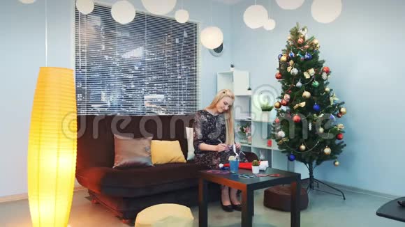 美丽的女人坐在靠近圣诞树的沙发上写圣诞信视频的预览图