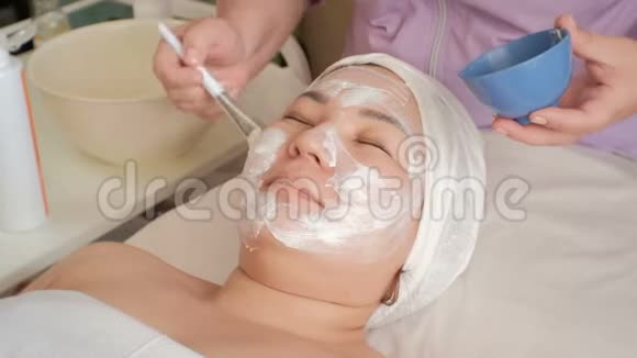 在美容院的亚洲女孩加速录像美容师用一种白色按摩霜涂在一个穆斯林妇女的脸上视频的预览图