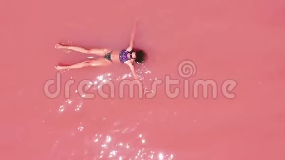 鸟瞰一个迷人的女人穿着比基尼漂浮在粉红色盐湖视频的预览图
