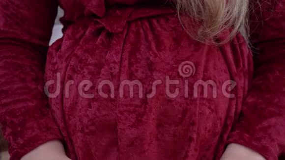 一个年轻的孕妇把婴儿套在肚子上穿着红裙子的女人玩弄着小毛裤视频的预览图