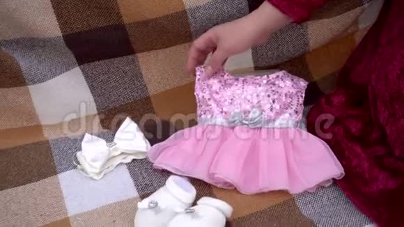 年轻的孕妇摸婴儿衣服穿着红裙子的女人玩弄着小毛裤视频的预览图