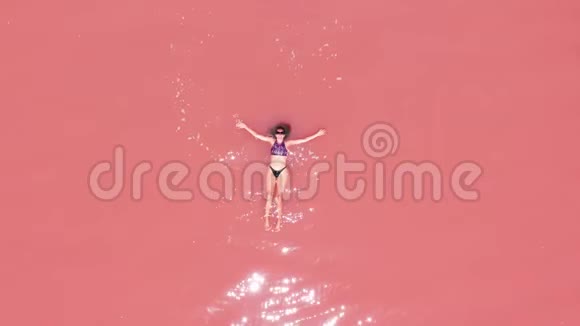 鸟瞰一个迷人的女人穿着比基尼漂浮在粉红色盐湖视频的预览图