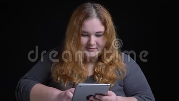 年轻的超重白种人女性在平板电脑上打字然后看着相机微笑的特写镜头视频的预览图