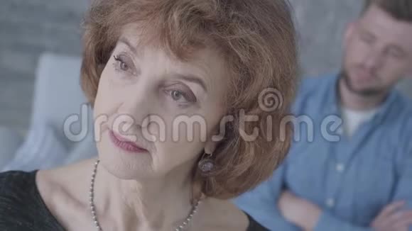 一个老态龙钟的成熟优雅悲伤的女人的脸紧紧地看着前景一个神经紧张的人模糊的身影视频的预览图