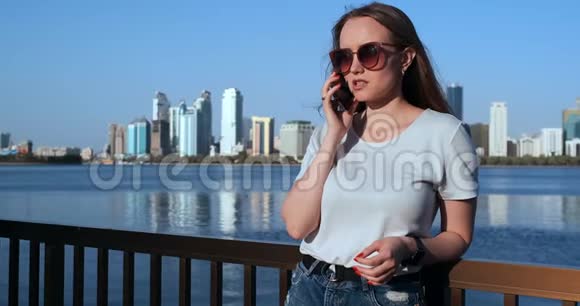 站在海滨的年轻漂亮女孩对着城市在打电话视频的预览图