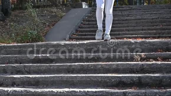 穿白色紧身裤和绿松石运动鞋的女性腿部特写公园里一个穿条纹裤子的女人下楼视频的预览图