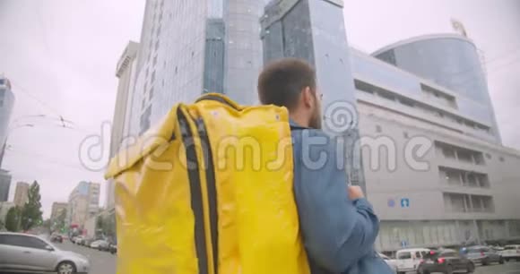 留着胡子的白种人送货员背着背包走在城市户外的街道上带着城市摩天大楼视频的预览图