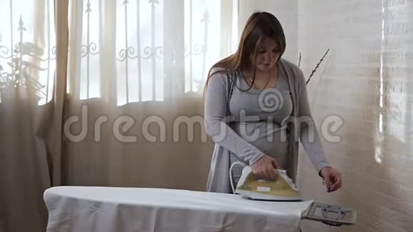 孤独可爱的年轻孕妇熨烫衣服视频的预览图