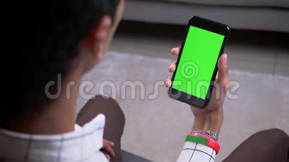 特写后景拍摄男性手拿着绿色屏幕的手机在公寓内打视频电话视频的预览图