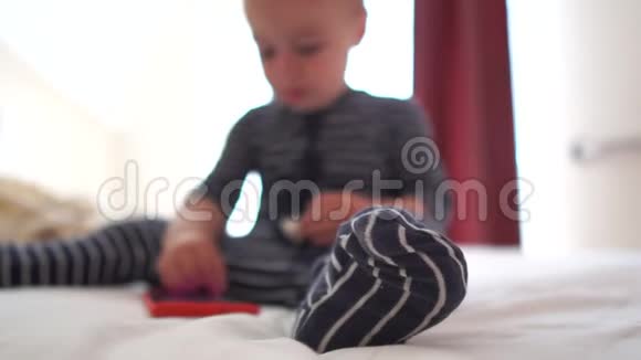 4K一个可爱的婴儿点击智能手机坐在大床上视频的预览图