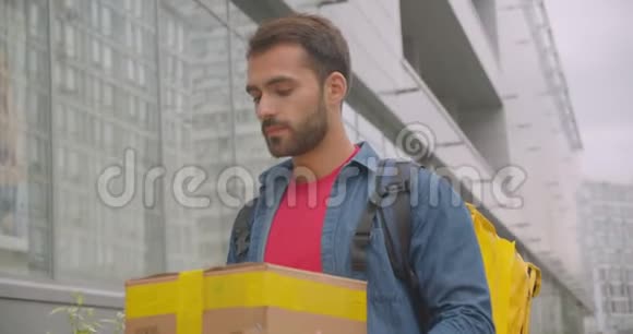 留着大胡子的白种人送货员的特写肖像背着背包在户外的城市里订购箱子视频的预览图