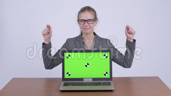 年轻快乐的金发女商人展示笔记本电脑在书桌前竖起大拇指视频的预览图