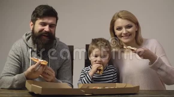 父亲母亲和他们的小儿子吃白色背景上孤立的美味披萨一家人享受美味的披萨视频的预览图
