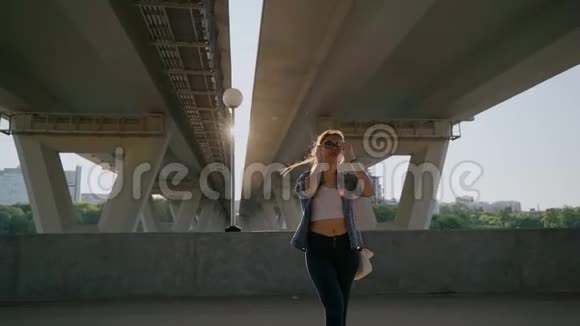 戴眼镜的女孩在汽车桥下为照相机摆姿势在风中飘扬的头发视频的预览图