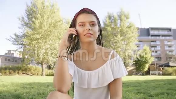 一个女孩坐在公园里写信息打电话黑发女人打电话在公园里漫游女孩打电话给她的朋友视频的预览图