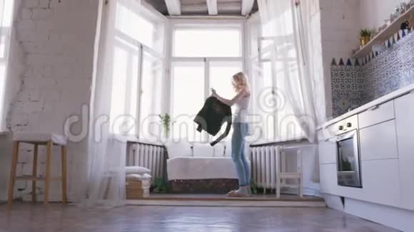 一位身穿白色t恤和牛仔裤的金发美女站在靠近窗户的地方穿着一件黑色的外套视频的预览图