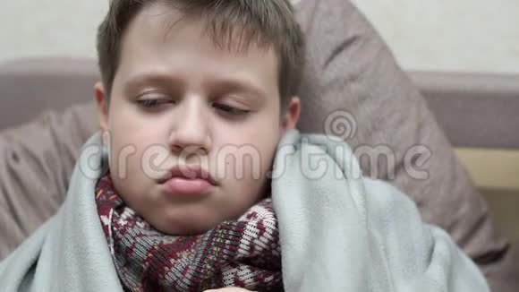 一个感冒男孩咳嗽他得了流感围着围巾坐在沙发上视频的预览图