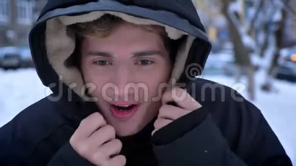 年轻英俊的白种人男性的特写镜头在雪地里穿着一件冬天的外套在户外微笑着冻僵了温暖了自己视频的预览图